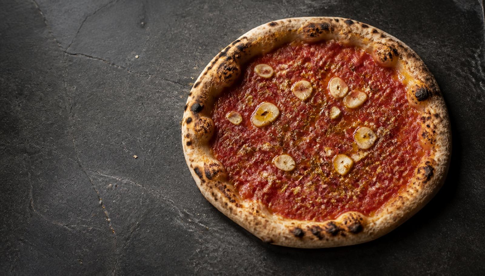 Pizza marinara con pomodoro, aglio a fette, origano e olio su un piano di ardesia scura